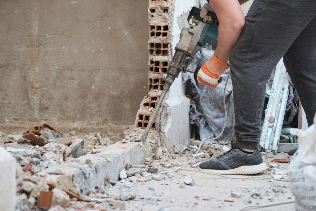 Unrecognizable man using a jackhammer to drill into wall.